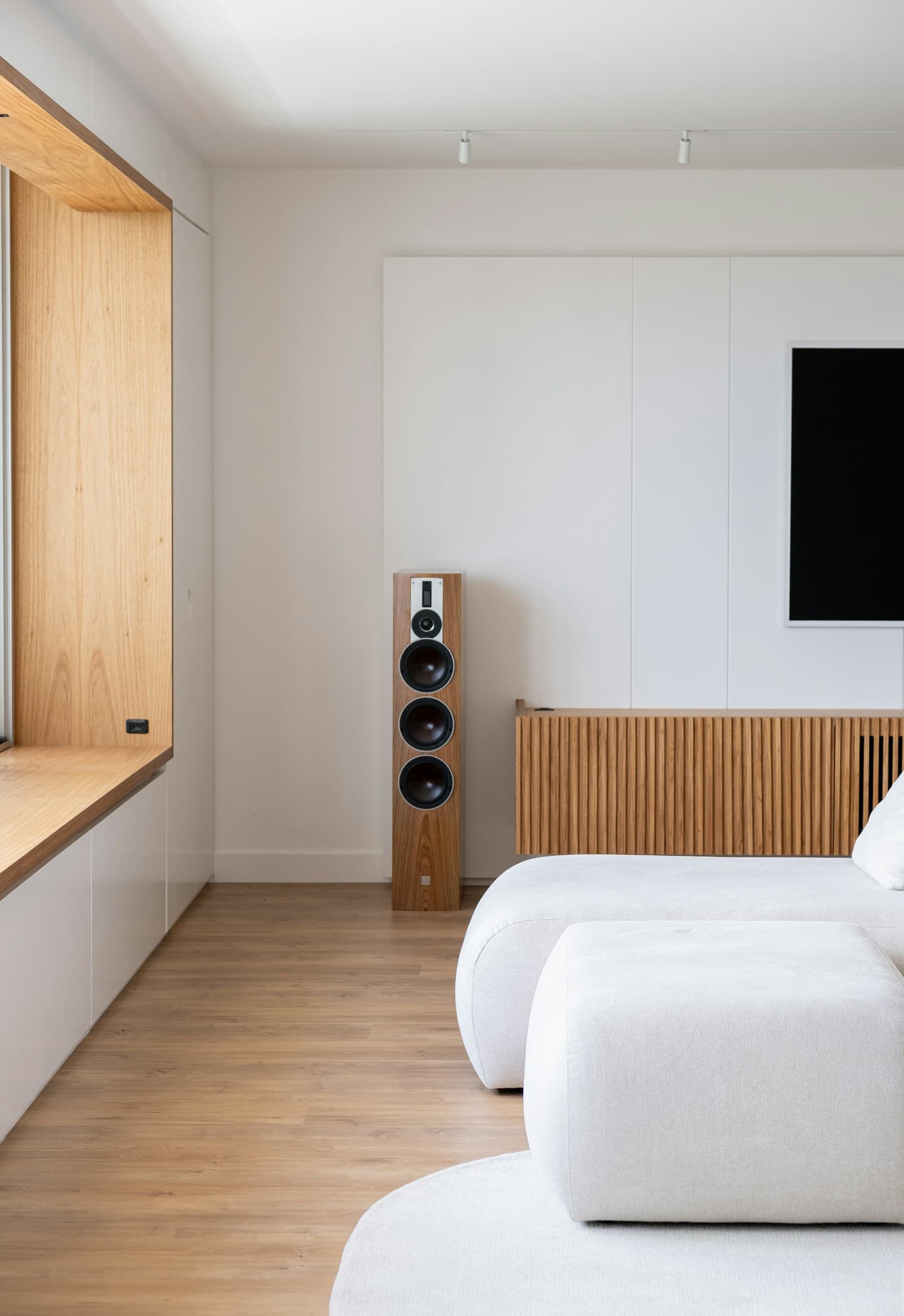 Minimalist white seating beside an oak-lined window, timber floor, and slatted oak media cabinet