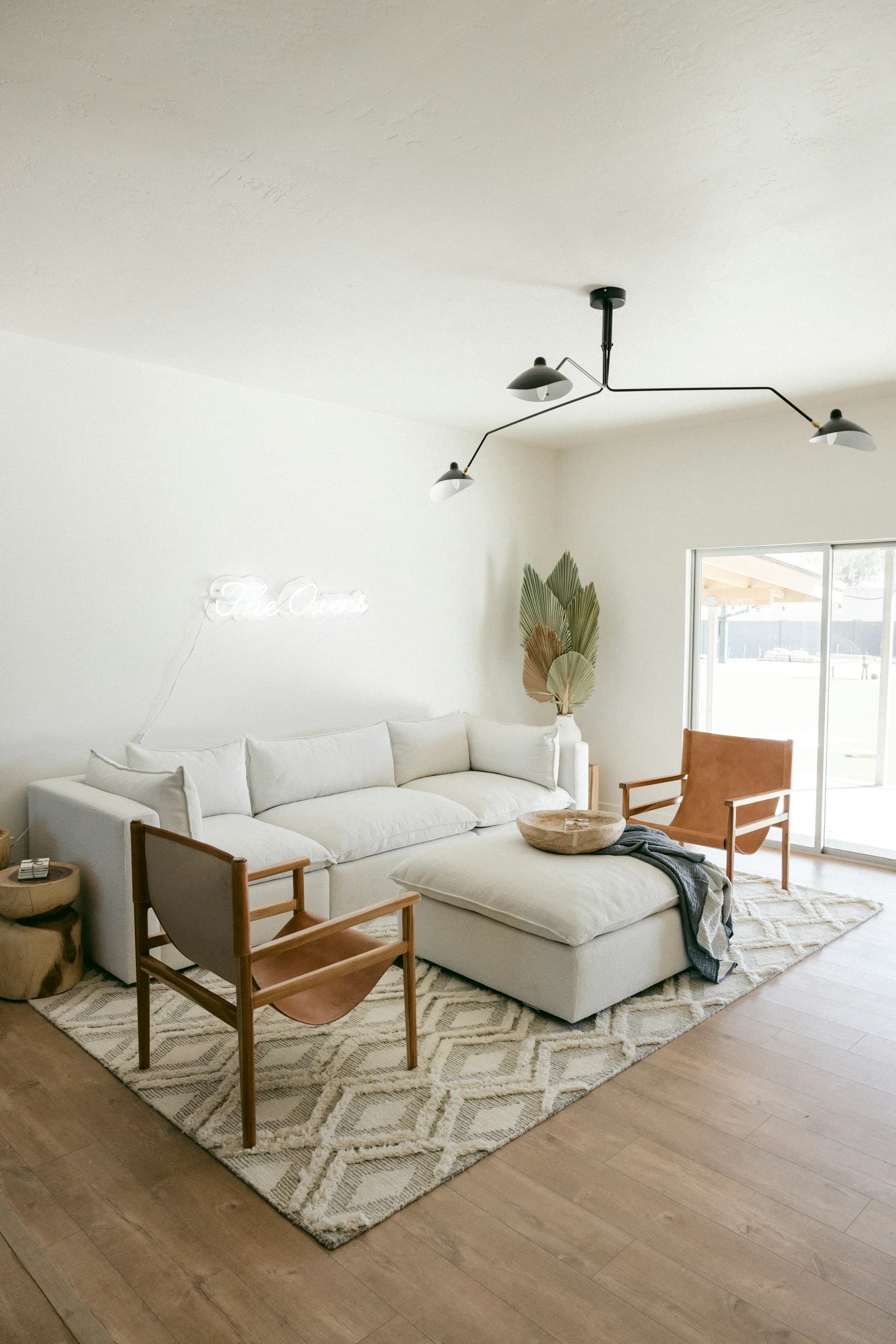 White sofa and ottoman with timber-framed leather chairs in a bright room with pale walls